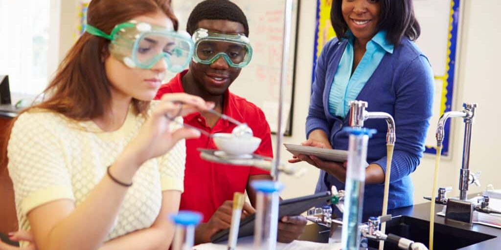 Pupils Carrying Out Experiment In Science Class Wearing Protective Glasses