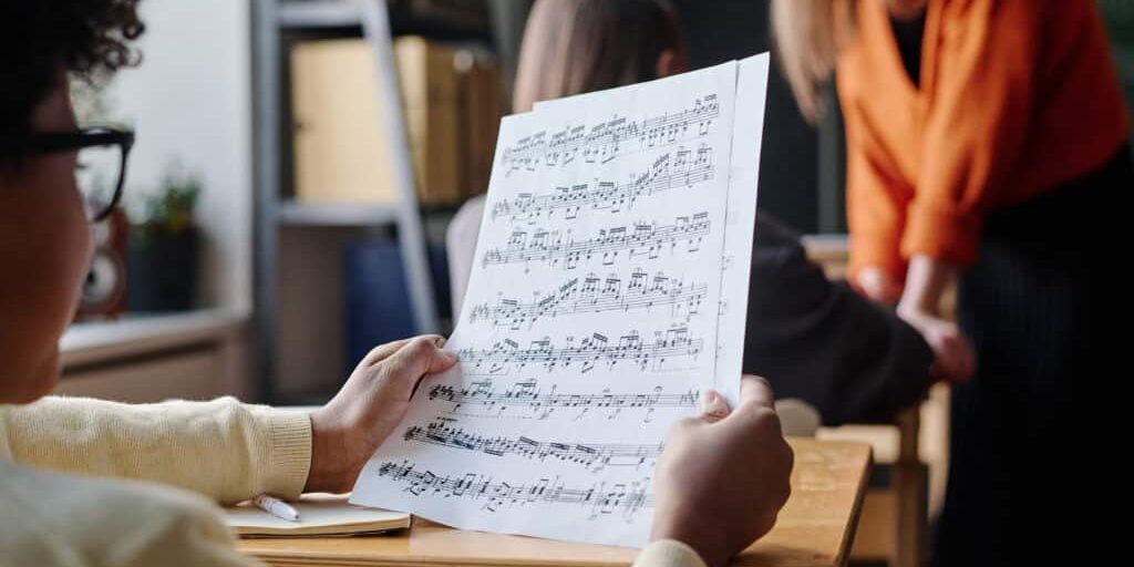 Selective focus shot of unrecognizable African American boy sitting at desk in classroom looking through sheet music paper during lesson